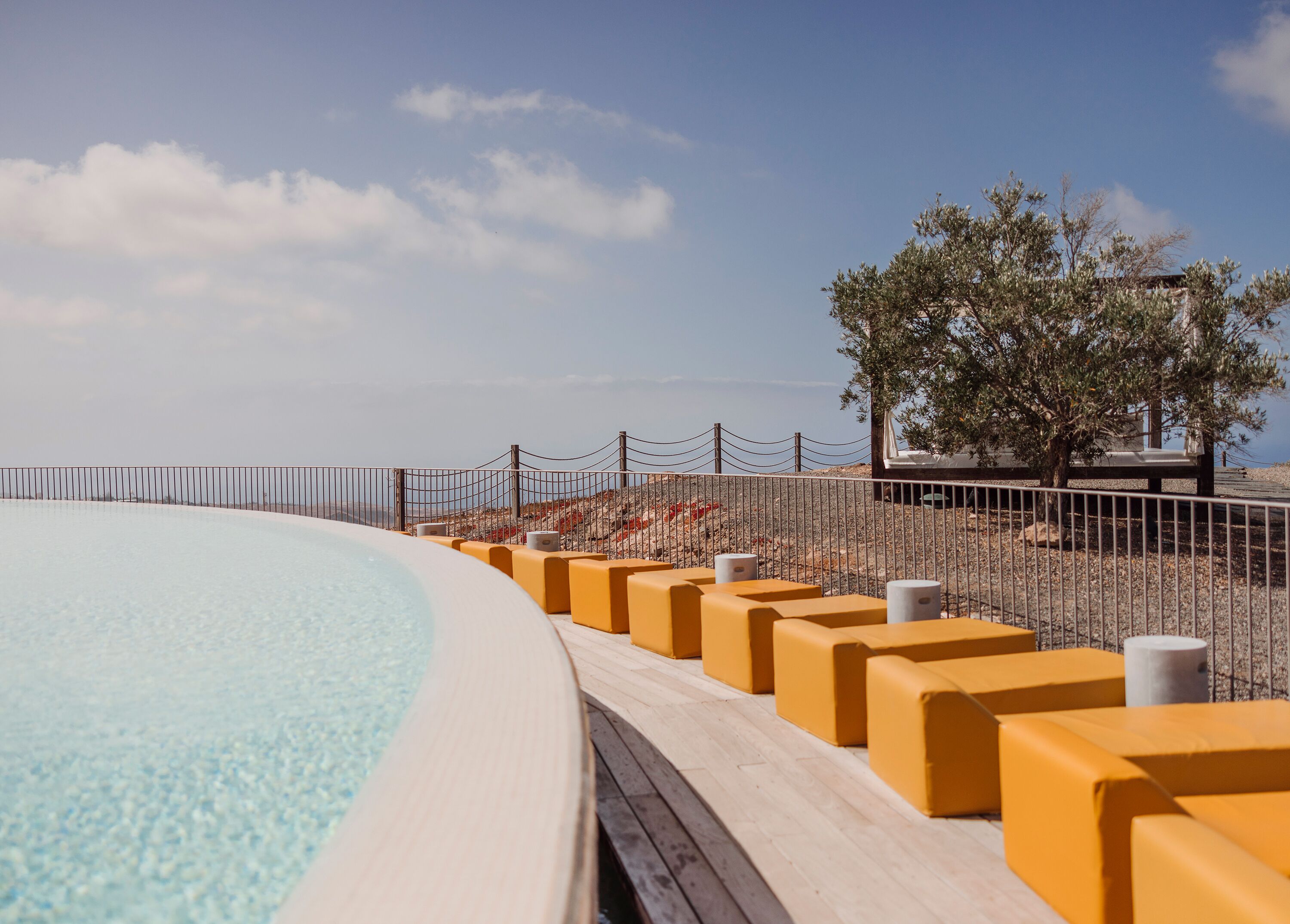 Una piscina con muelle de madera y barreras amarillas, rodeada por una valla y árboles.