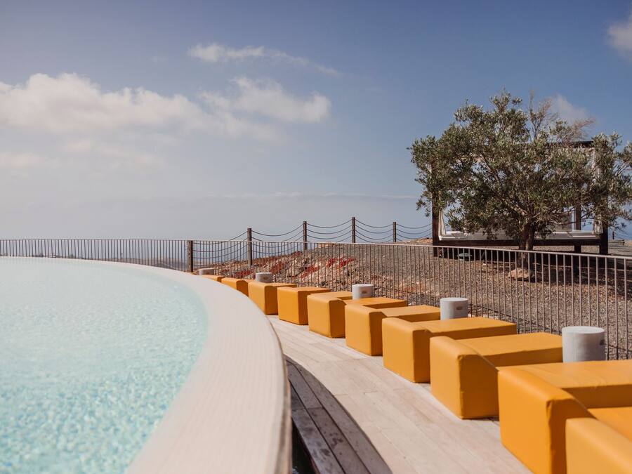 Una piscina con muelle de madera y barreras amarillas, rodeada por una valla y árboles.