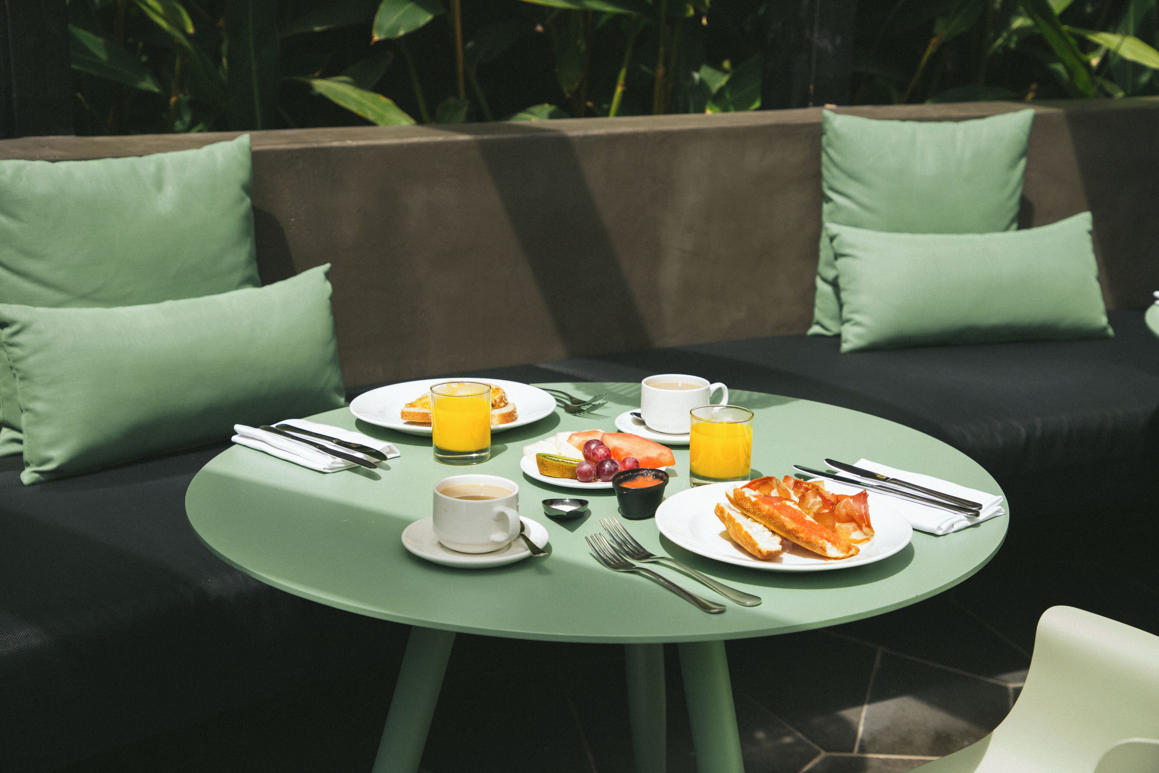 Una mesa redonda con alimentos para el desayuno, una taza de café y un vaso de zumo de naranja.
