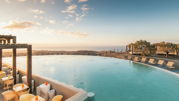 A infinity pool with lounge chairs and tables, overlooking a scenic view of hills and the ocean. - Salobre Hotel Resort & Serenity (San Bartolomé de Tirajana)