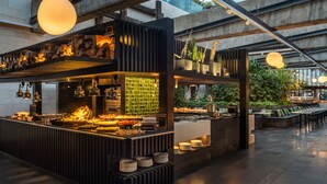 An outdoor dining area with a modern design, featuring a central cooking station, seating arrangements, and a view of the surrounding urban landscape. - Salobre Hotel Resort & Serenity (San Bartolomé de Tirajana)