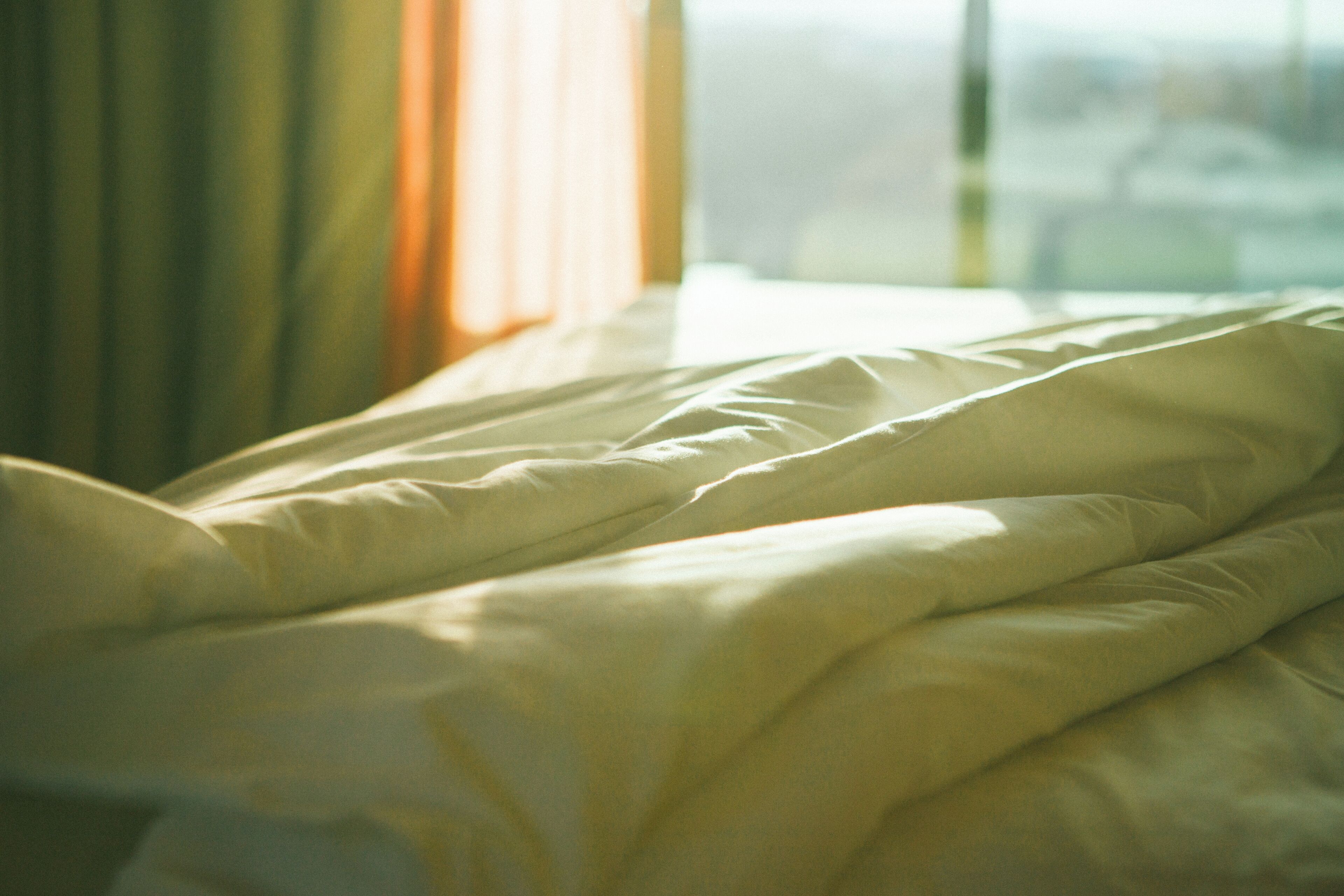Una cama con ropa blanca y una ventana con cortinas.