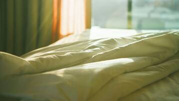 Una cama con ropa blanca y una ventana con cortinas.