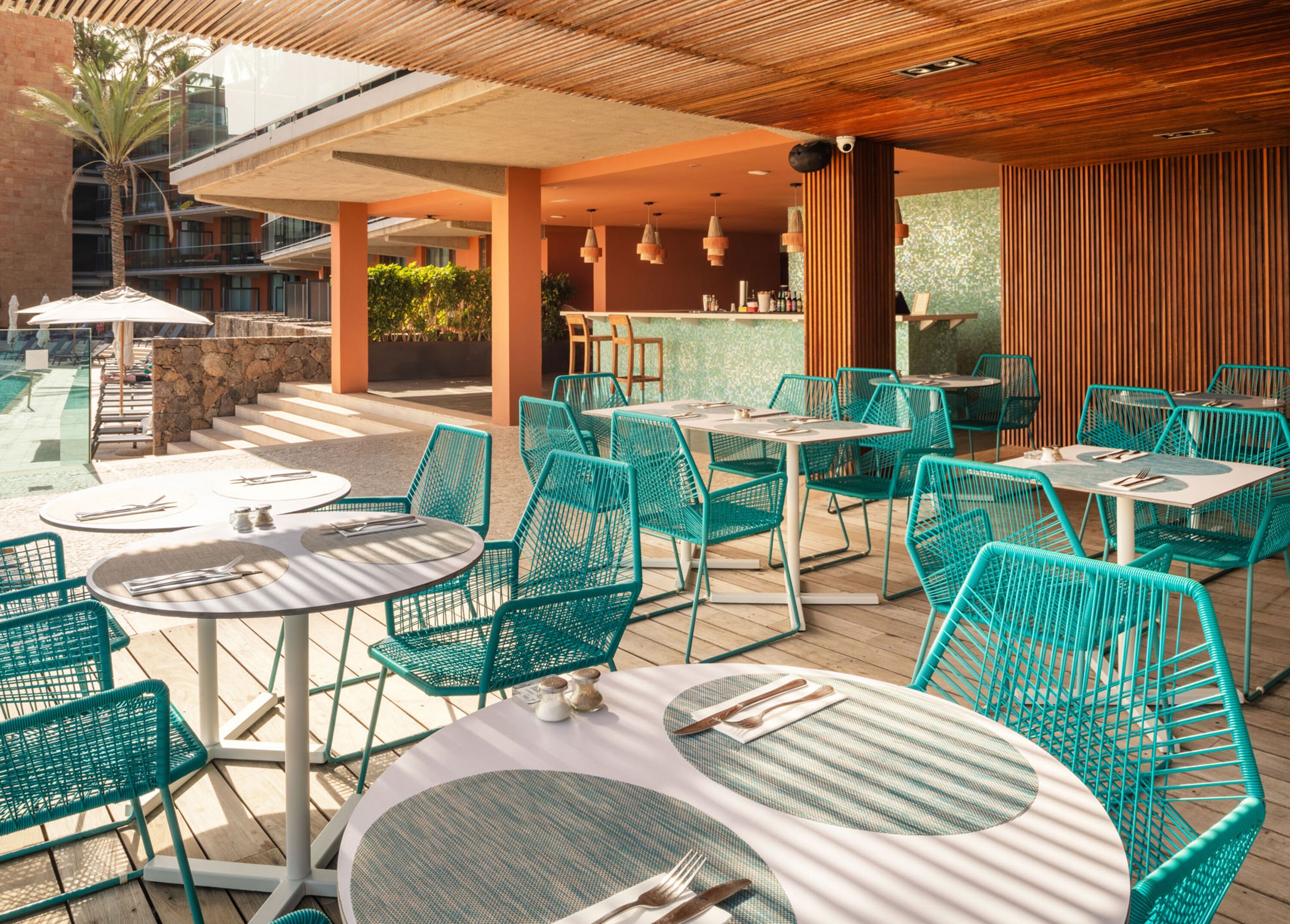 Un espace extérieur aménagé en terrasse, avec des tables rondes et des chaises vertes, un bar et une piscine en arrière-plan.