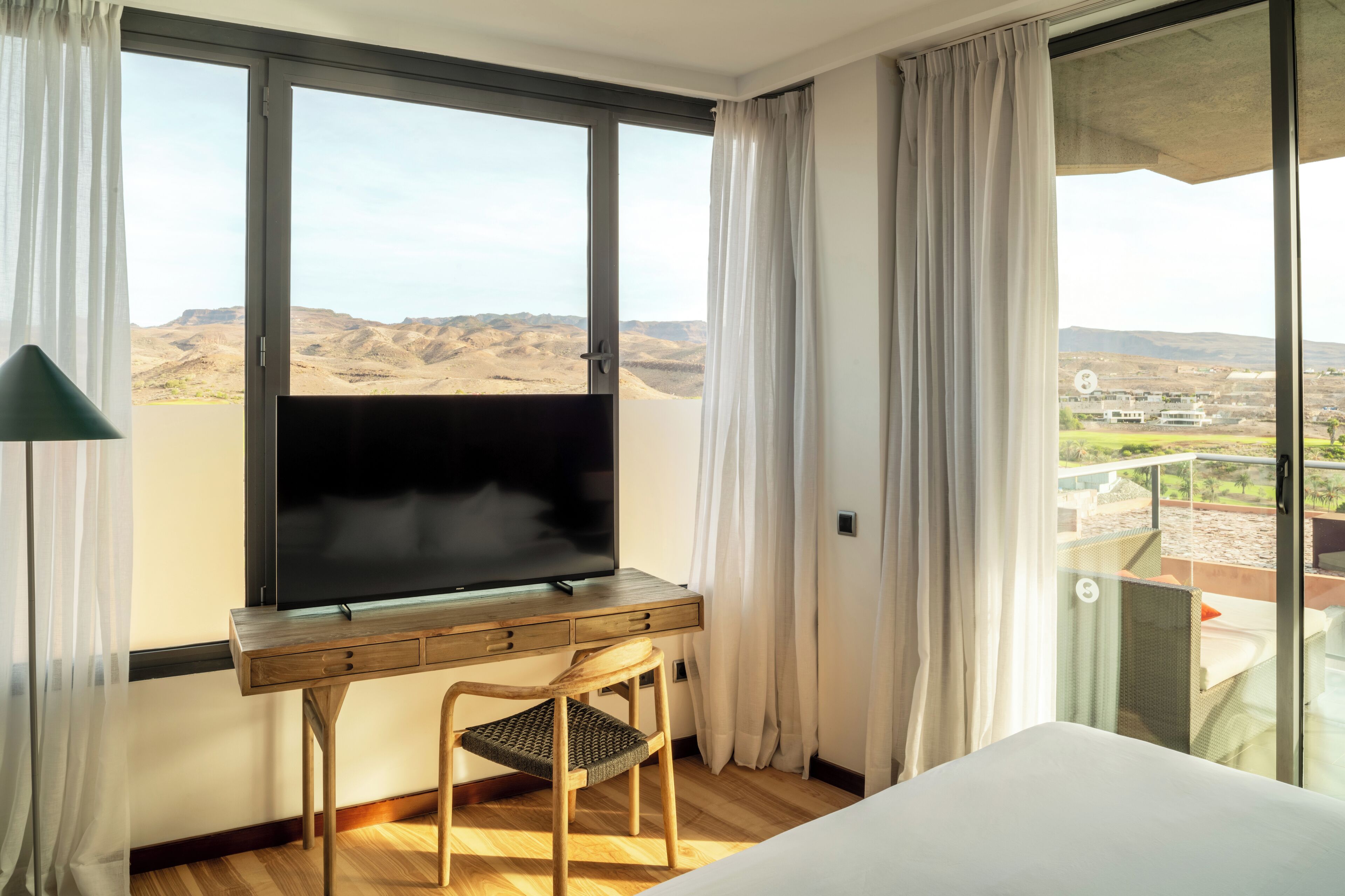 Une chambre d’hôtel avec une grande fenêtre, un bureau avec une chaise et un lit.