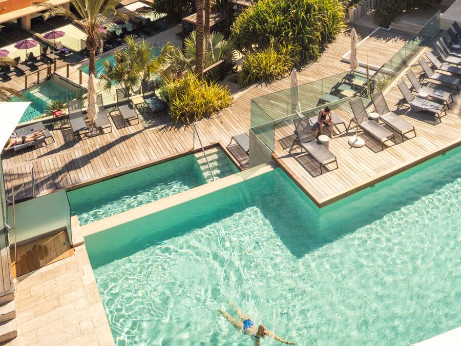 An aerial view of a resort with two swimming pools, sun loungers, and a wooden deck.