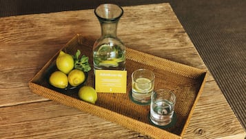 A wicker tray with lemons, a bottle, and two shot glasses on a wooden table.