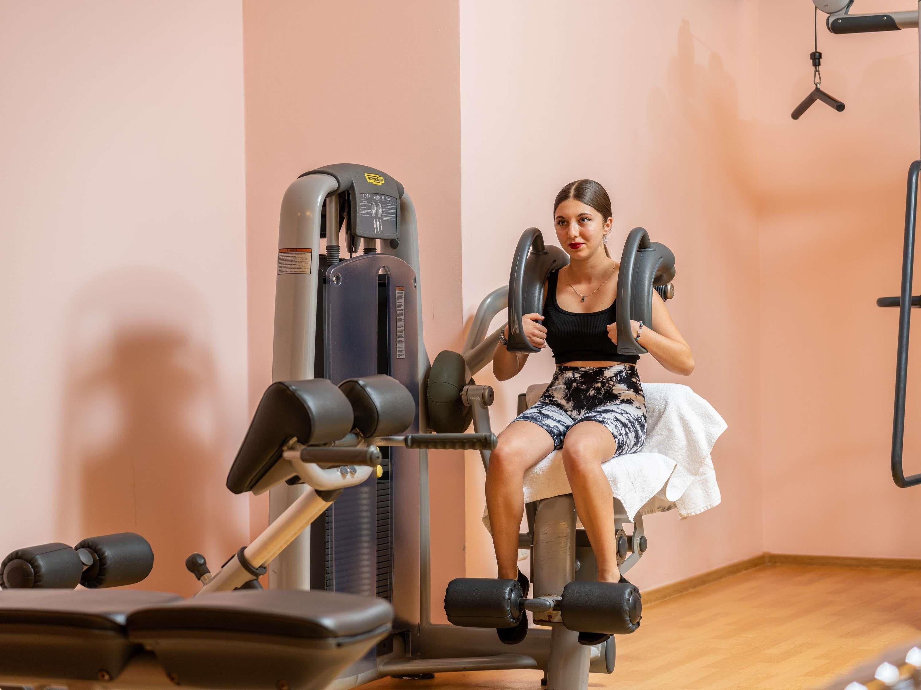 A person using a leg press machine in a gym with a wooden floor and a pink wall.