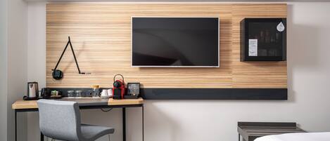 Una habitación de hotel moderna con una pared de acento de madera, un televisor de pantalla plana, un escritorio con una silla y una cama con un cojín rojo decorativo.