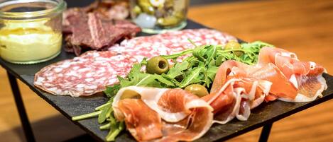 Una tabla de embutidos con diversos tipos de carne, aceitunas y vegetales, acompañada de pequeños frascos de salsas.