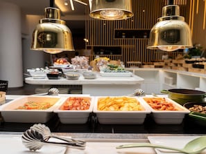 A buffet with various dishes, a white table, and gold pendant lights.
