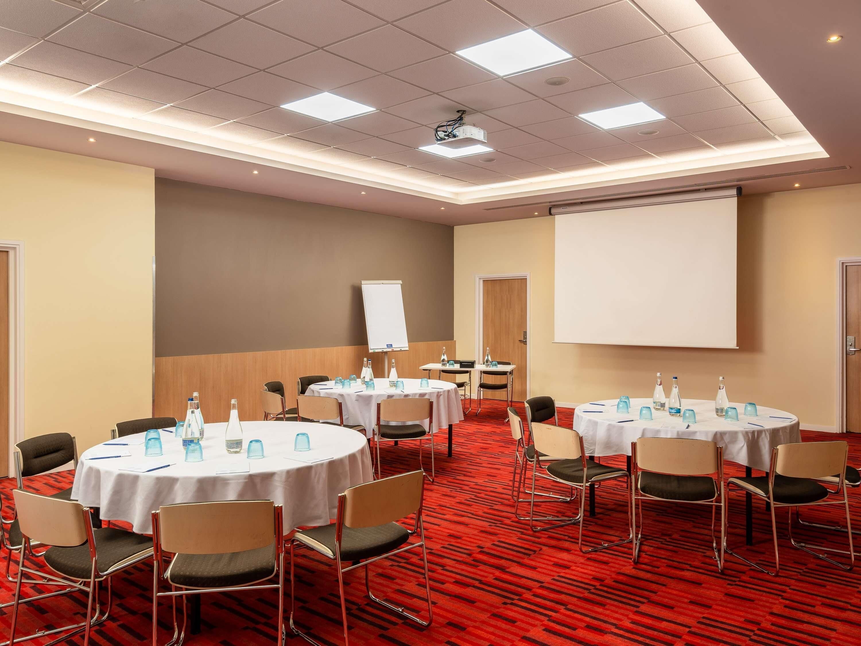 A conference room with multiple tables, chairs, a projector, and a whiteboard.