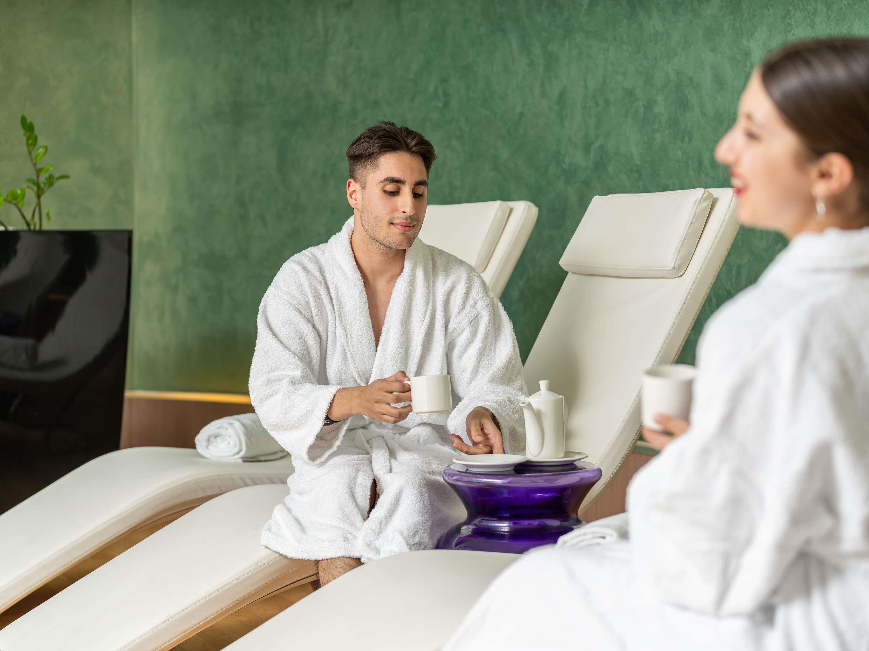 Ein Wellnessraum mit Massage-Sessel, Fernseher und einem kleinen Tisch mit Tasse und Untertasse.