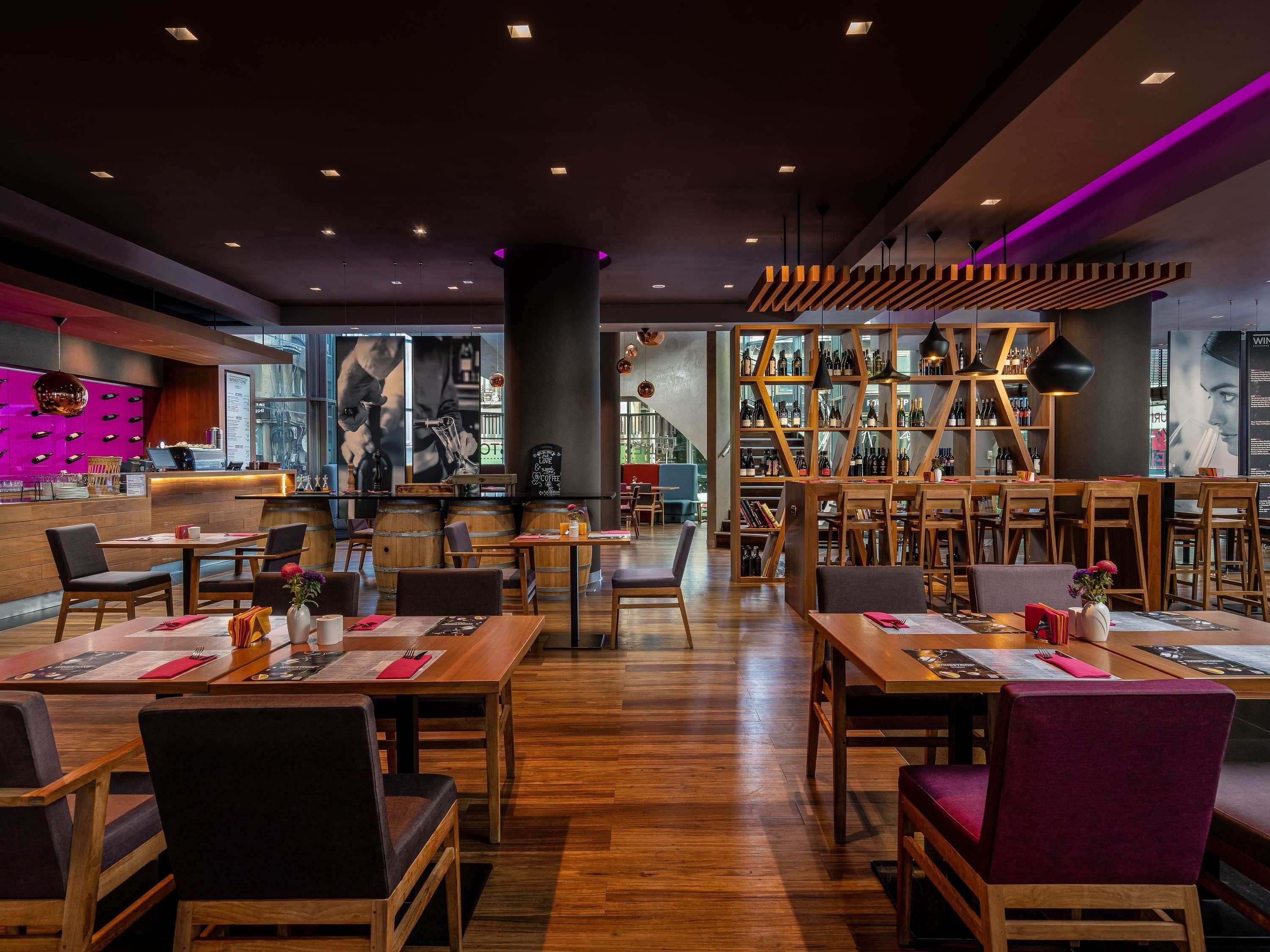 Un restaurante moderno con mesas y sillas de madera, una zona de bar y una vitrina para vinos.