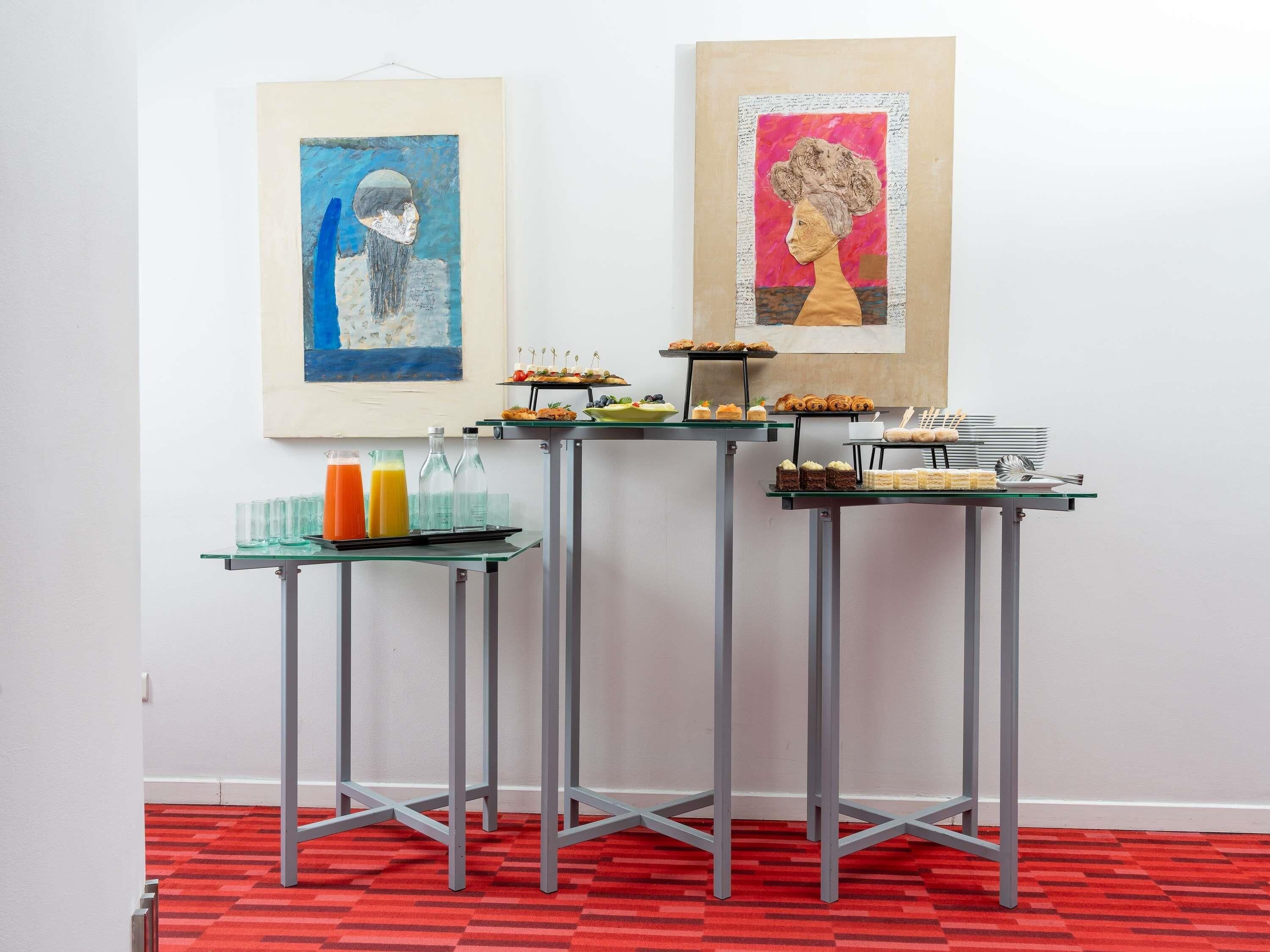 A room with a red carpet, a table with food and drinks, and two framed artworks on the wall.