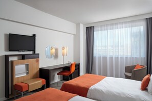 A hotel room with two beds, a desk, a chair, a TV, and a large window with curtains. - Novotel Bucharest City Centre (Bucharest)