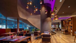 Een modern interieur met houten tafels en stoelen, een grote boekenkast en hanglampen.