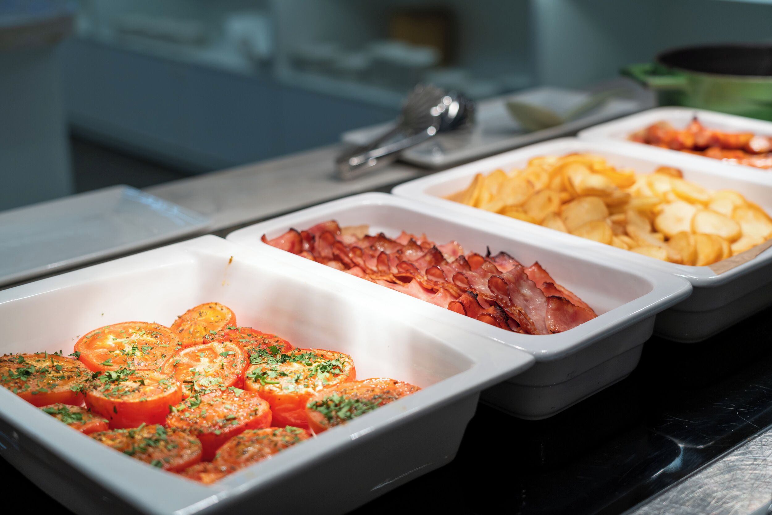 A buffet with various food options including sliced tomatoes, bacon, and potatoes.