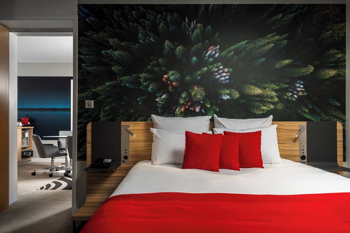 A hotel room with a bed, a desk, and a chair. There is a large window with a view of a body of water.