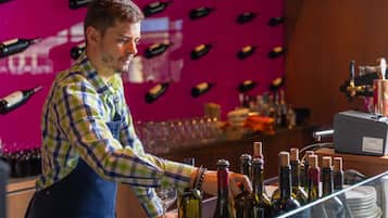 A bar area with a bartender preparing drinks. There are multiple bottles of wine and a wine glass on the counter.