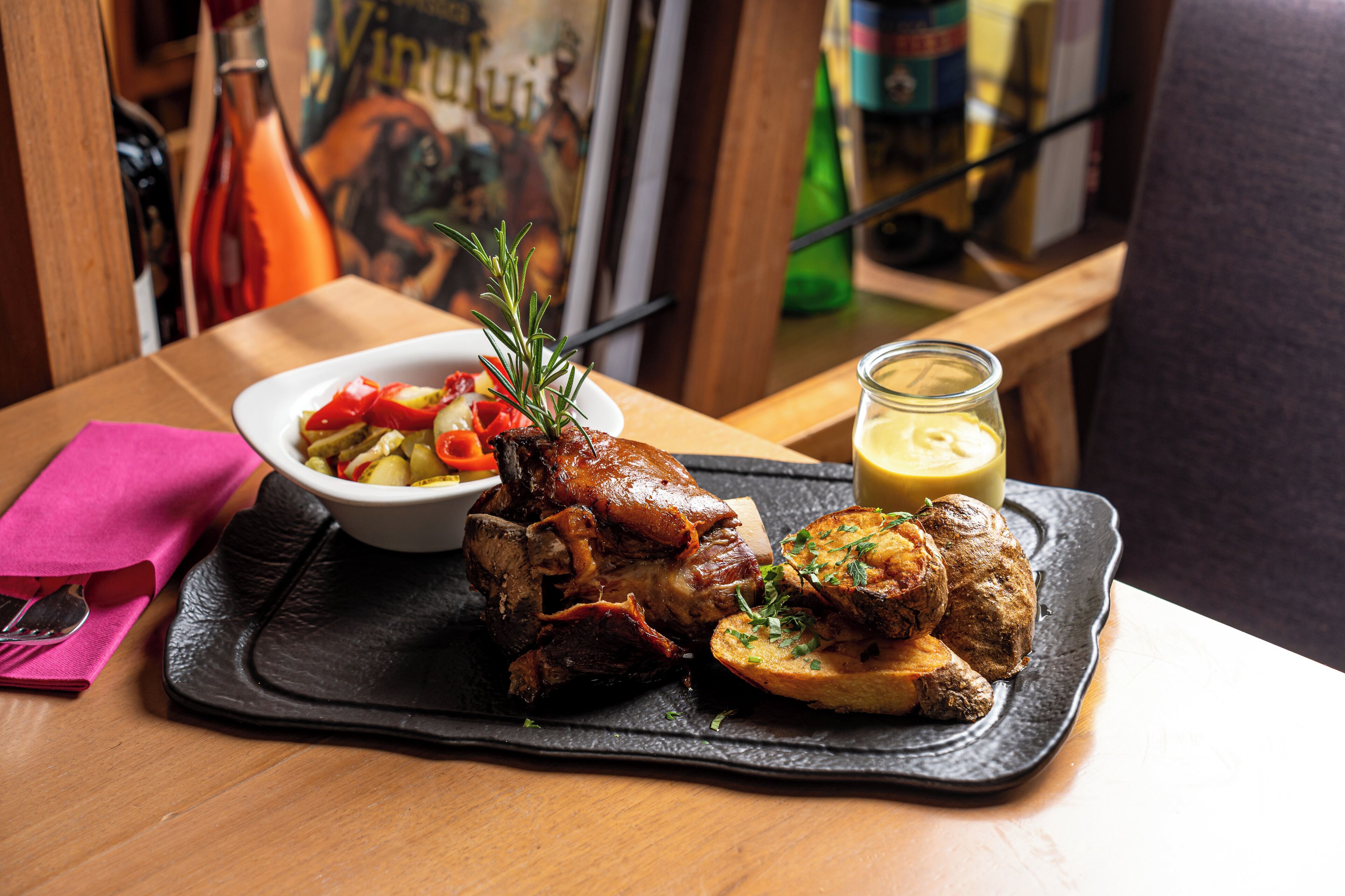 A meal with roasted meat, vegetables, and a sauce on a black tray.
