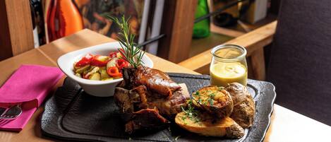 A meal with roasted meat, vegetables, and a sauce on a black tray.