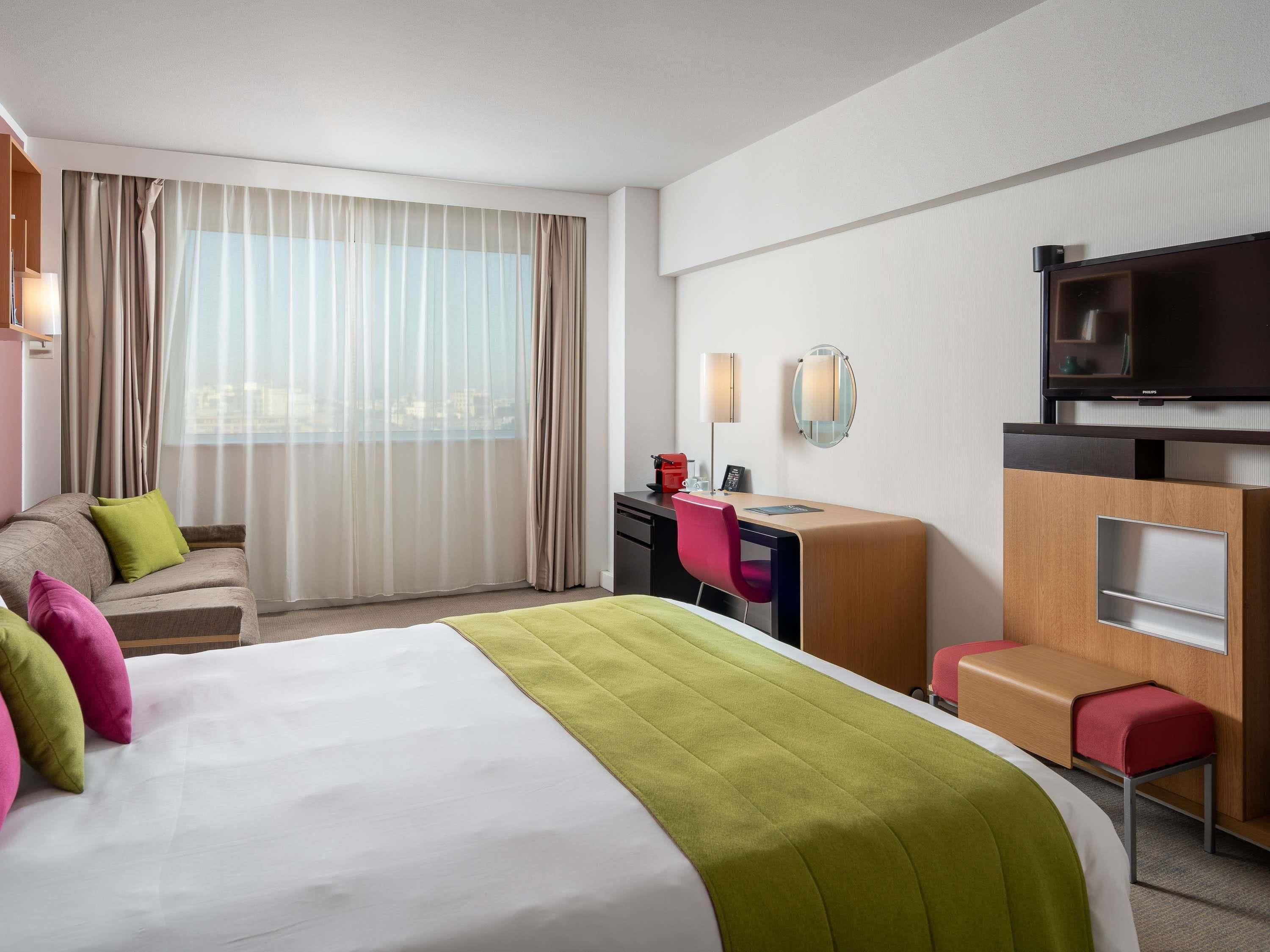 A hotel room with a bed, a desk, a chair, a television, and a window with curtains.