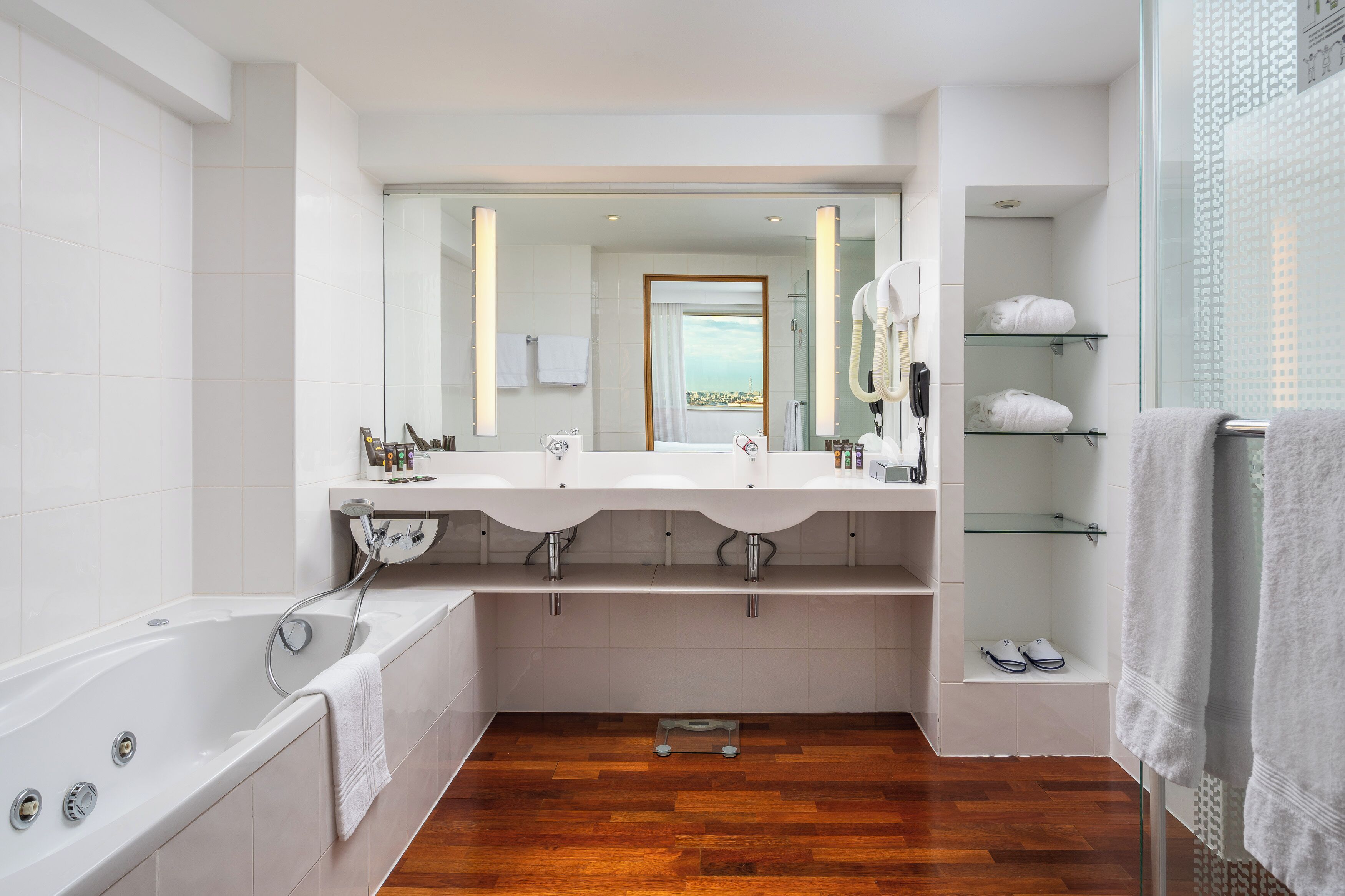 A modern bathroom with a large bathtub, two sinks, and a glass shower enclosure.