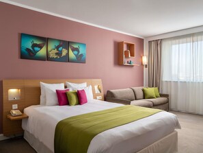 A hotel room with a bed, a sofa, a wall-mounted shelf, and artwork. - Novotel Bucharest City Centre (Bucharest)