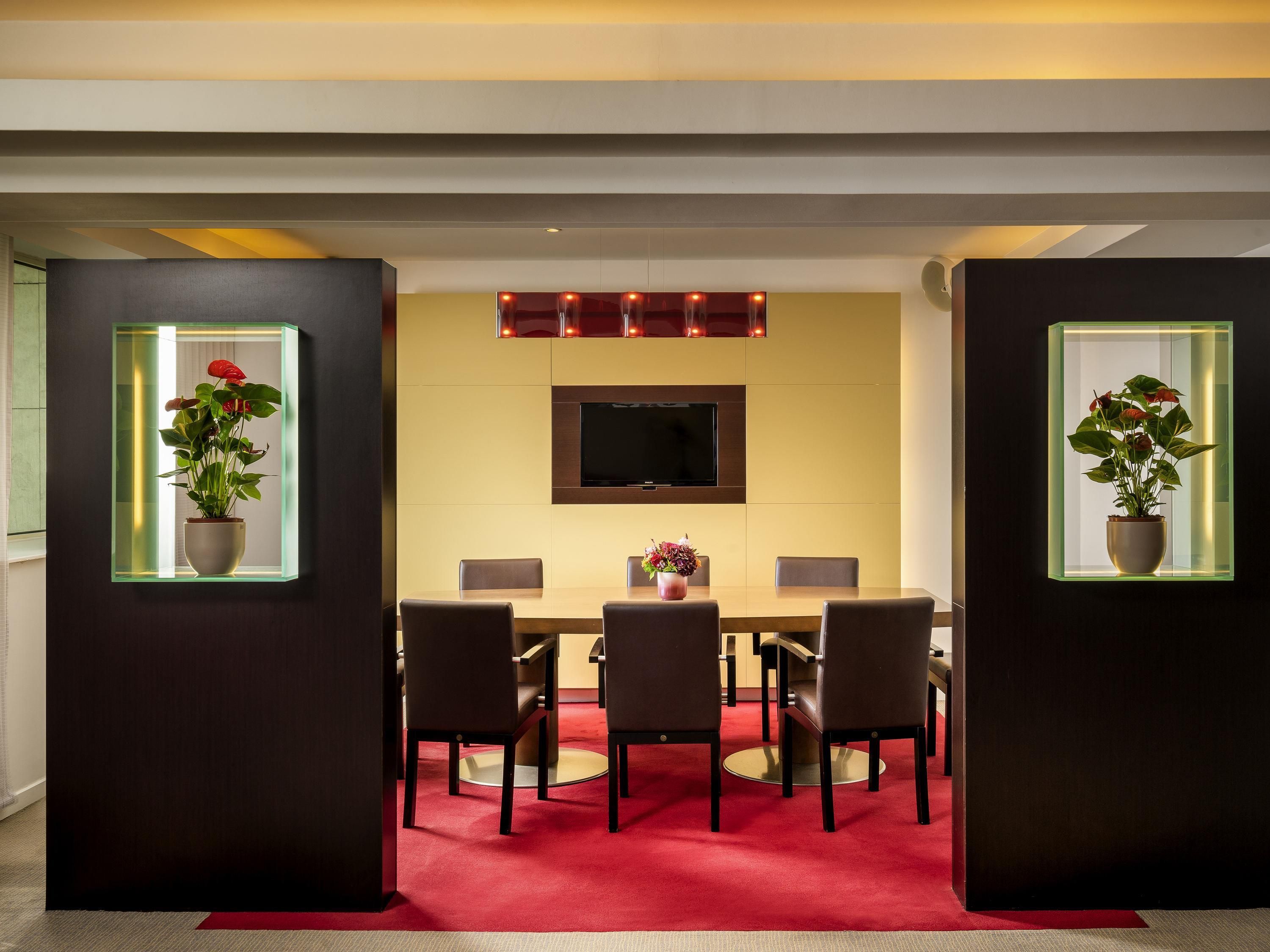 A modern dining area with a table, chairs, a TV, and potted plants.