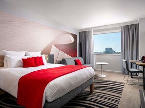 A modern hotel room with a large bed, a small table, and a view of the city. - Novotel Bucharest City Centre (Bucharest)