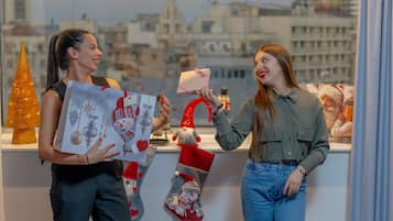 Two people exchanging gifts at a counter with a city view, a Christmas tree, and festive decorations.