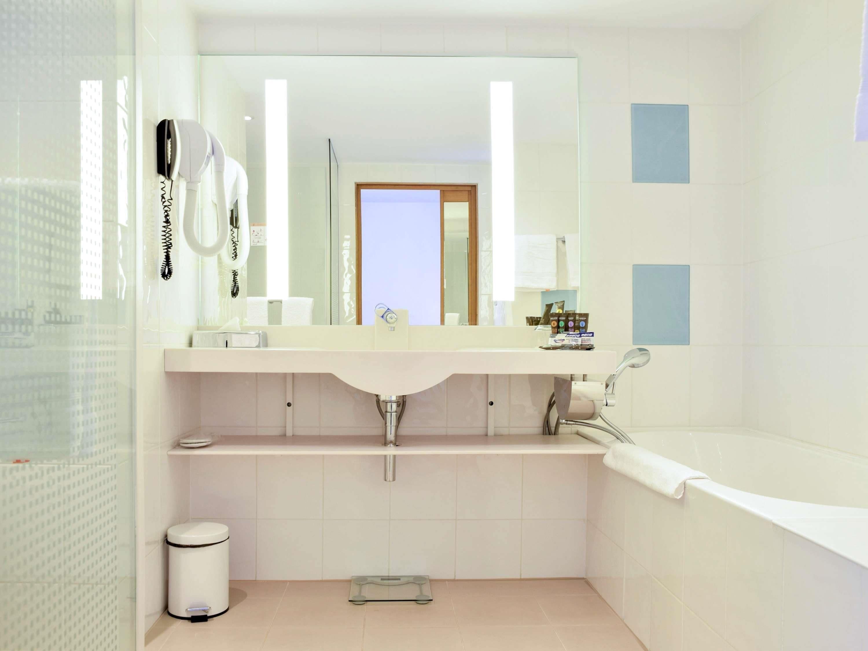 A modern bathroom with a large mirror, a white sink, a bathtub, and a toilet.