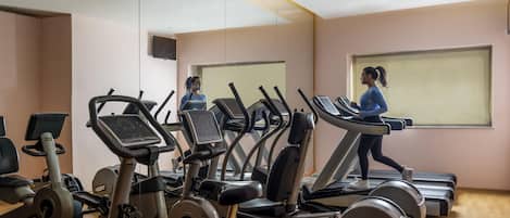 A gym with multiple treadmills and exercise bikes, a large mirror, and a window with blinds.