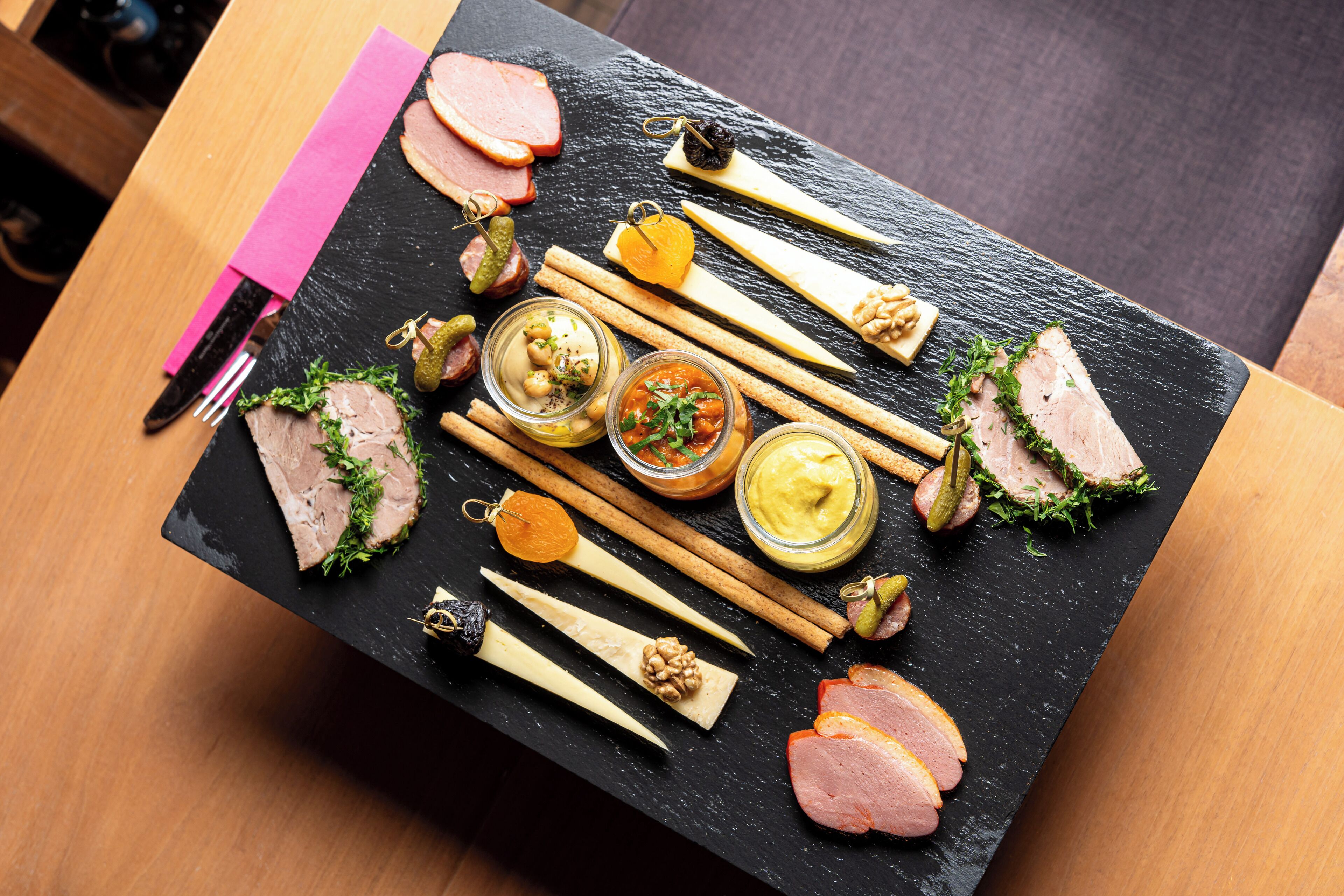 A black slate board with various food items including meats, cheeses, and condiments.