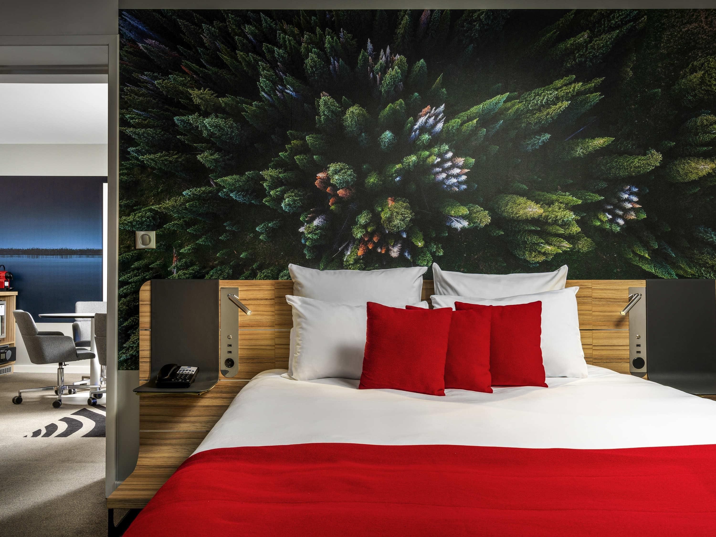 A hotel room with a bed, a desk, and a view of a forest through a window.
