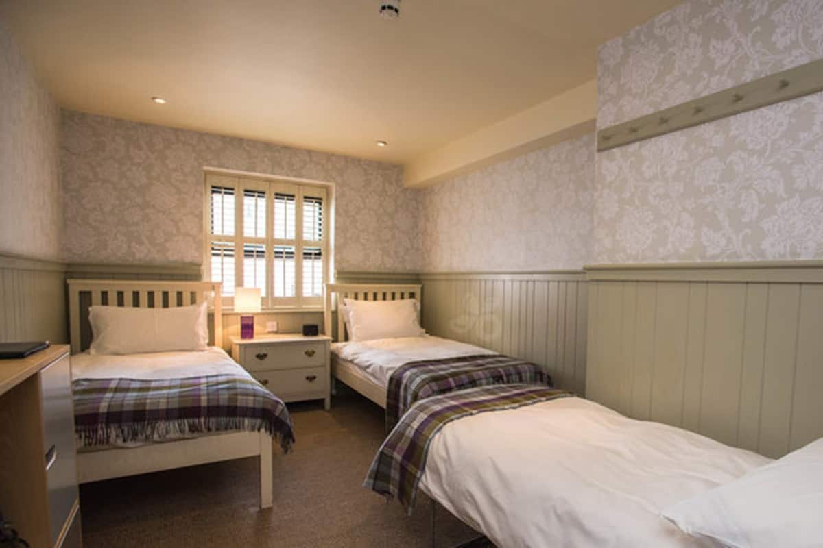 Ein Schlafzimmer mit zwei Einzelbetten, einem Nachttisch mit Lampe und einem Fenster mit Rollläden.