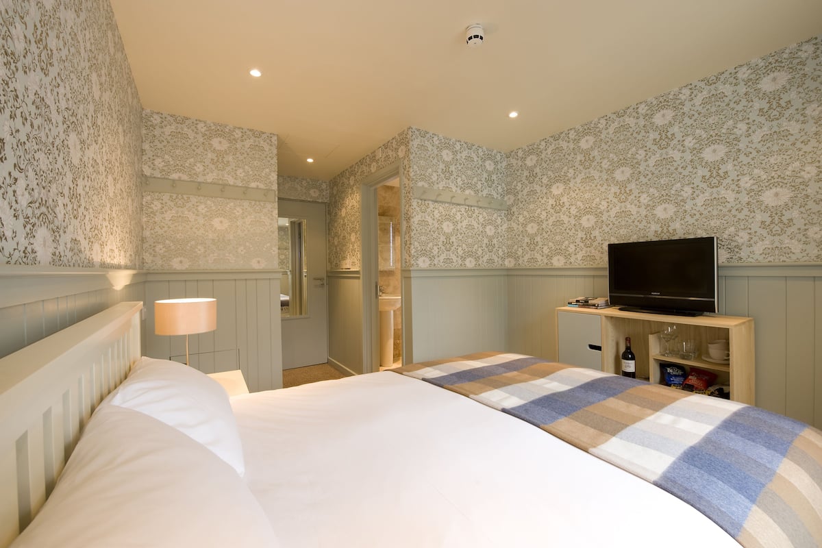 Ein Hotelzimmer mit Bett, Fernseher auf einem Holzständer, einer Weinflasche und einem kleinen Schrank.