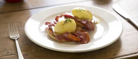 A plate of eggs Benedict with poached eggs, bacon, and hollandaise sauce on a wooden table.