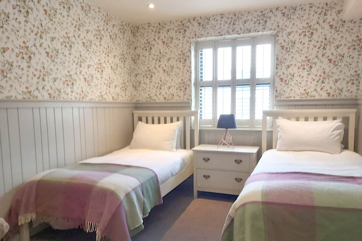 Ein Schlafzimmer mit zwei Einzelbetten, einem Nachttisch mit Lampe und blumigem Wandpapier.