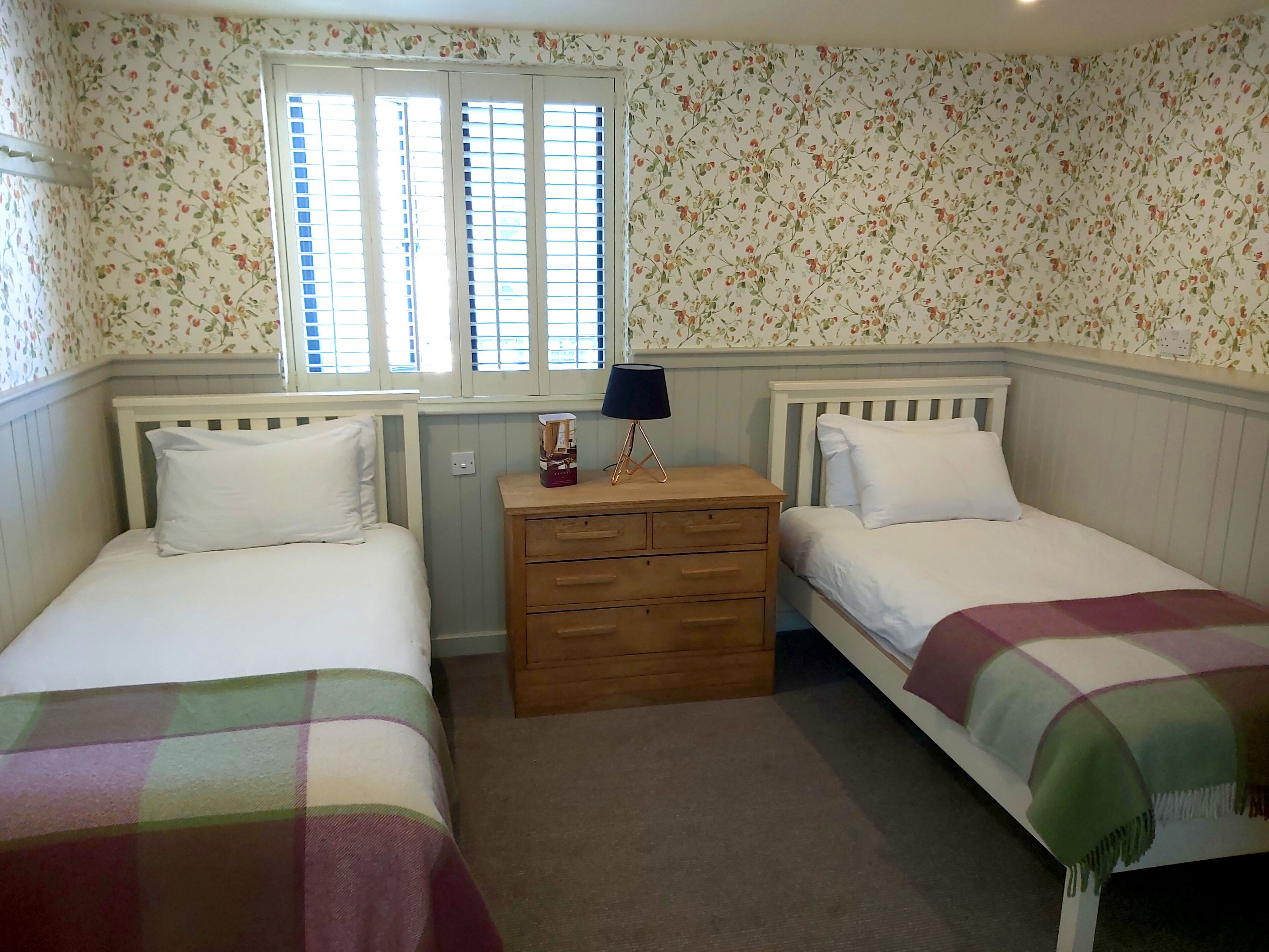 A bedroom with two single beds, a wooden dresser, and a window with shutters.