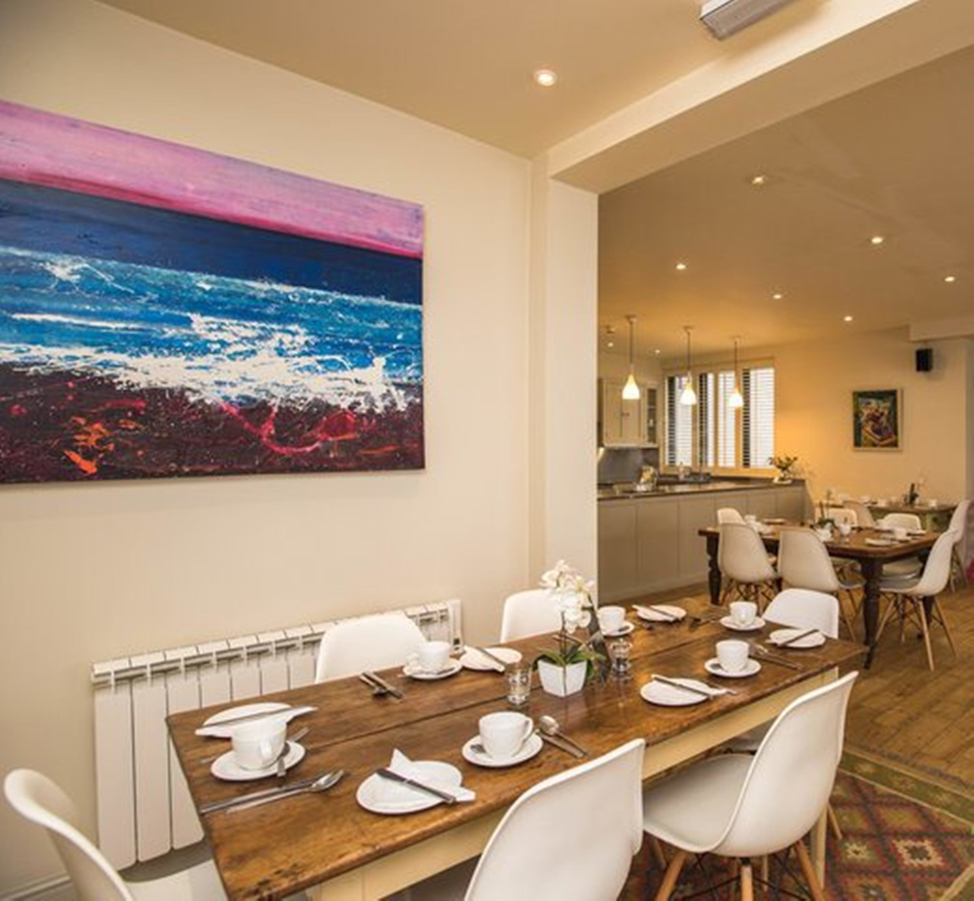 A dining area with a wooden table set for a meal, white chairs, and a large abstract painting on the wall.