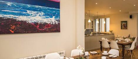 A dining area with a wooden table set for a meal, white chairs, and a large abstract painting on the wall.