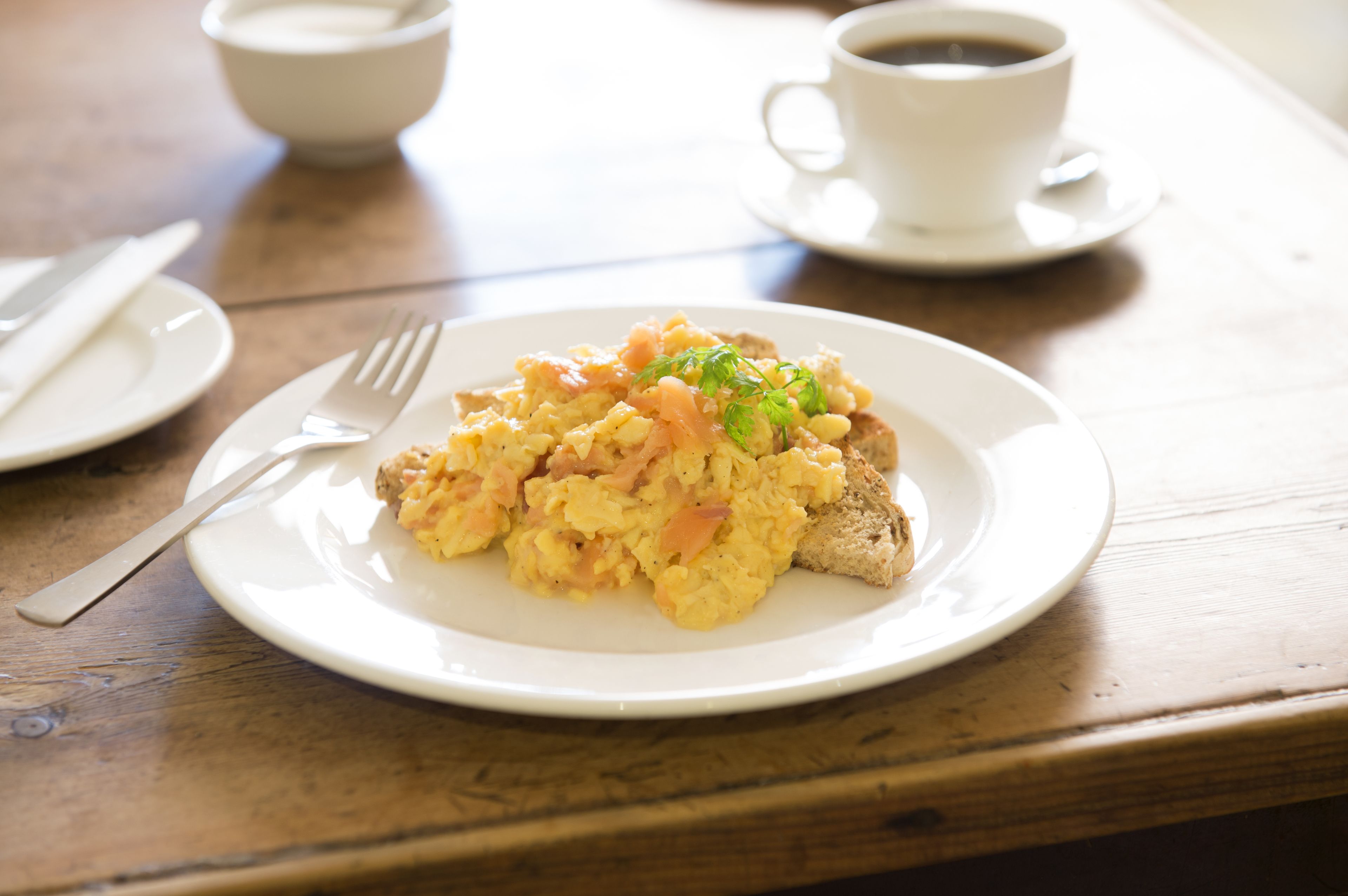 A breakfast setting with scrambled eggs, toast, and a cup of coffee on a wooden table.