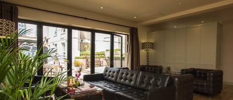A spacious living room with a large black leather sofa, a wooden coffee table, and a potted plant.