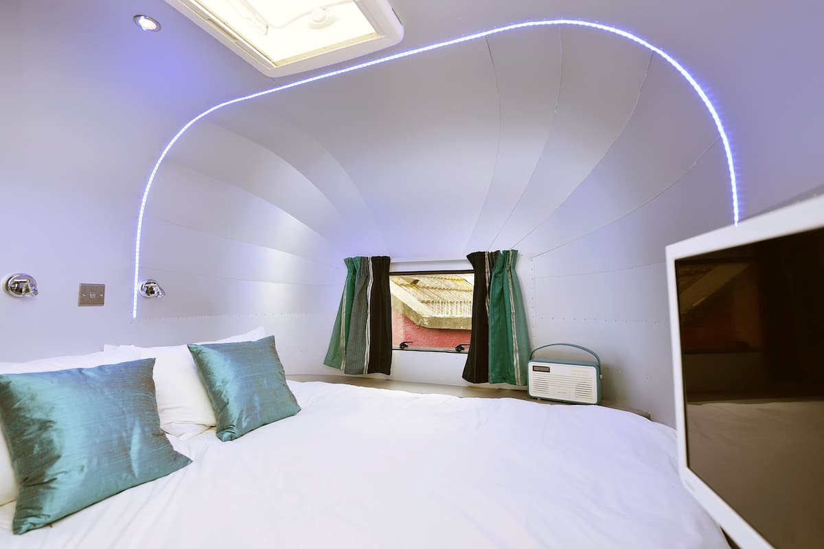 Ein Schlafzimmer mit Bett, türkisfarbenen Kissen, einem Oberlicht und einem Radio.