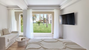 A modern hotel room with a large window, a flat-screen TV, a sofa, a round coffee table, and a decorative rug.