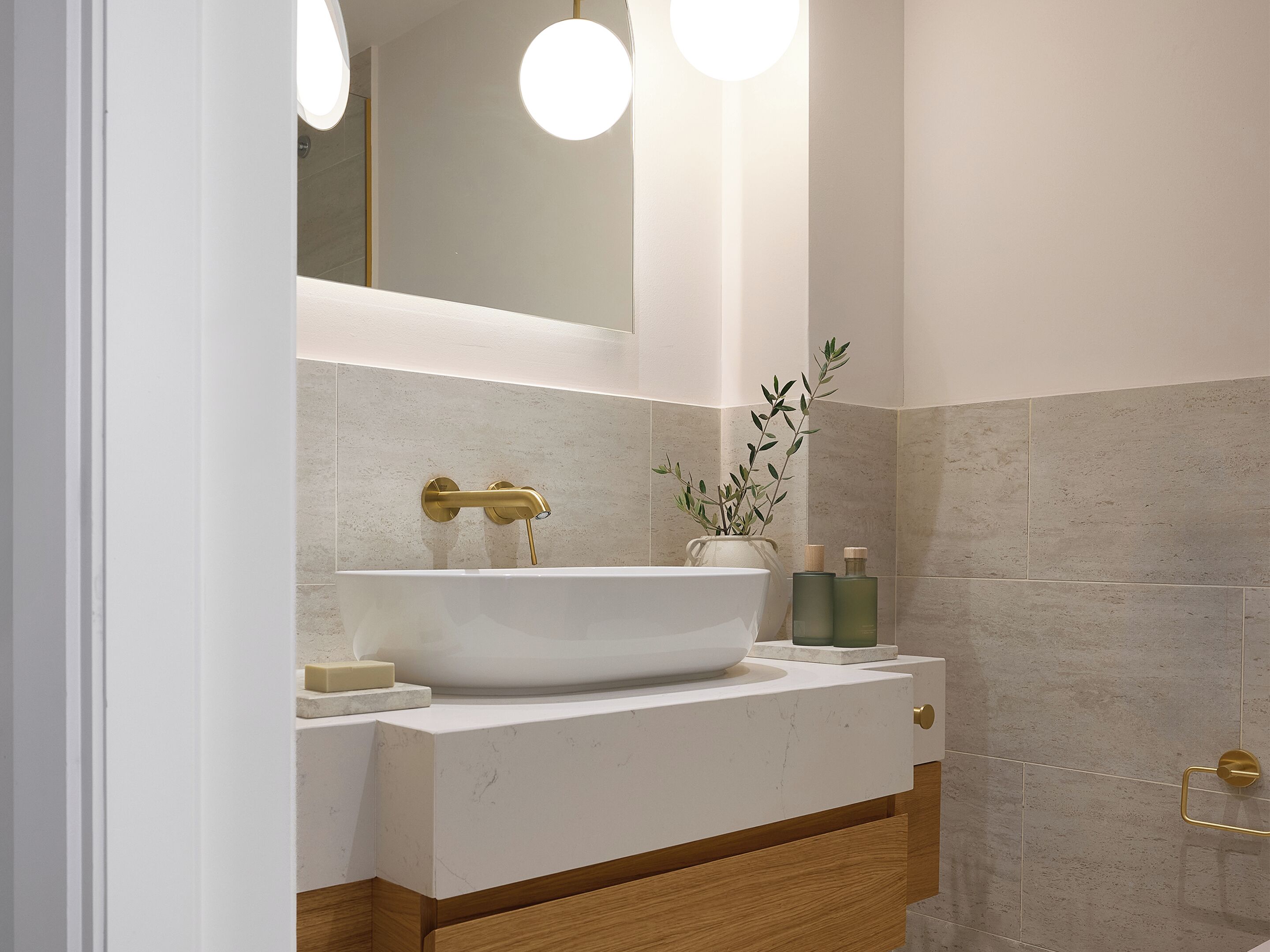 Ein modernes Badezimmer mit einem weißen Waschbecken, goldenen Armaturen und einem Spiegel darüber.