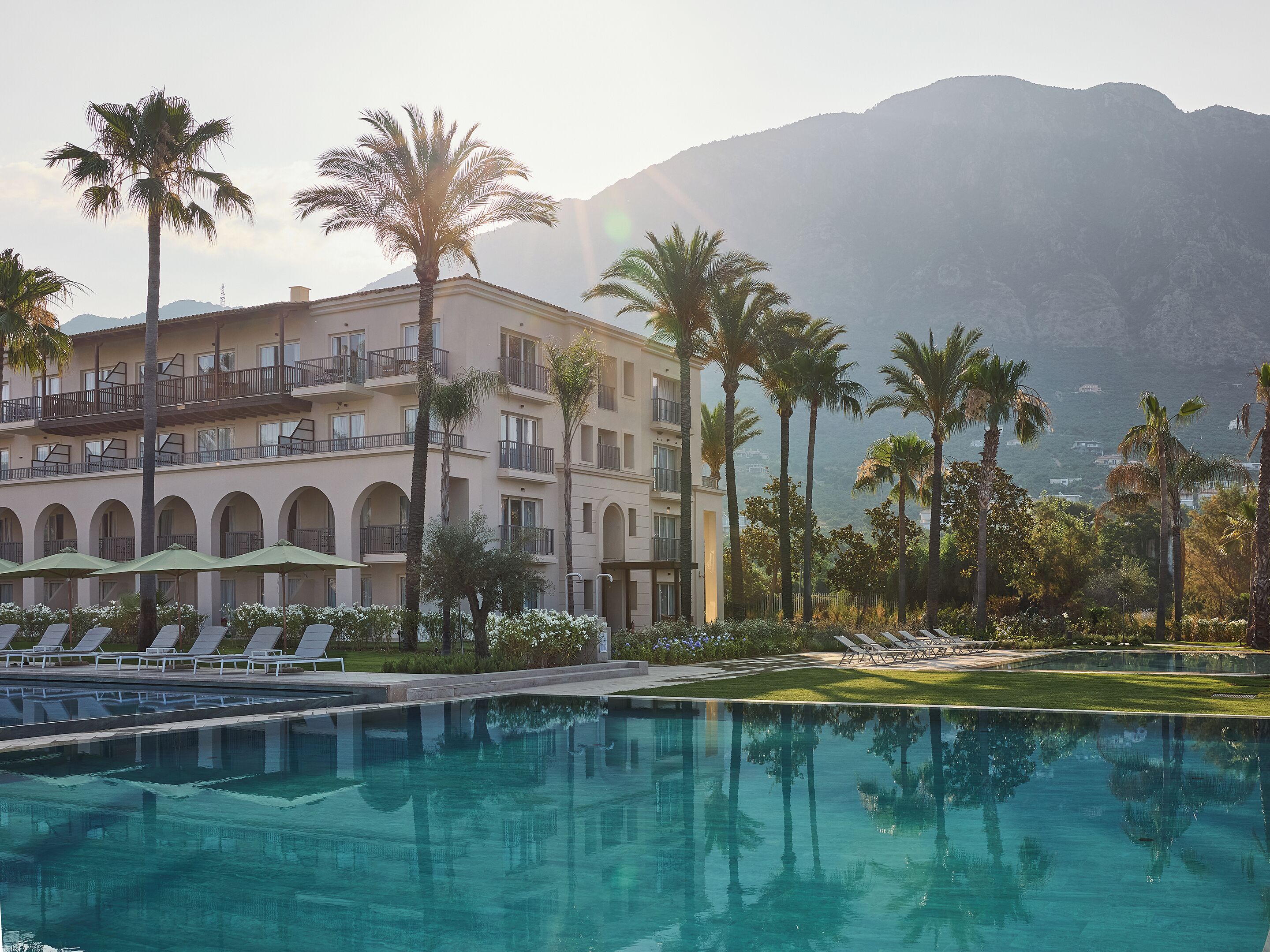 Un hotel con piscina, palmeras y montañas al fondo.