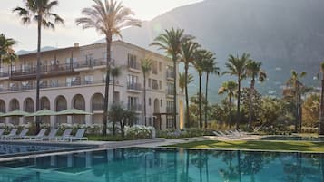 Un hotel con piscina, palmeras y montañas al fondo.
